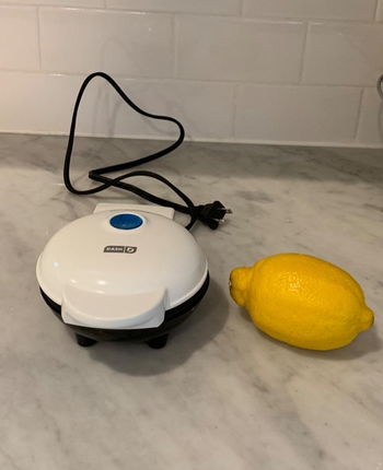 reviewer image of the small waffle maker in white, next to a lemon, showing the small size