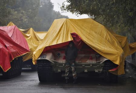 An Indian army soldier stands guard next to the parked tanks that will be participating in the upcoming Republic Day parade, as it rains in New Delhi January 22, 2015. REUTERS/Adnan Abidi