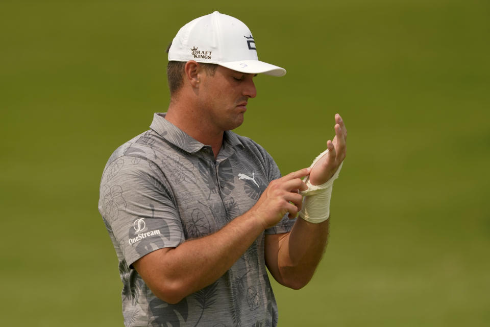 Bryson Dechambeau looks at his injured arm on the eighth hole during a practice round for the PGA Championship golf tournament, Tuesday, May 17, 2022, in Tulsa, Okla. (AP Photo/Matt York)
