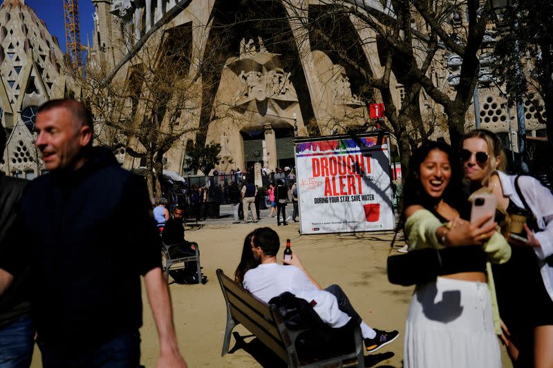 Turistas junto a un cartel en la Basílica de la Sagrada Familia que alerta de la grave sequía en la región noreste de España e insta a ahorrar agua debido a los bajos niveles de los embalses, en un momento en que Cataluña declara el estado de emergencia, en Barcelona, España