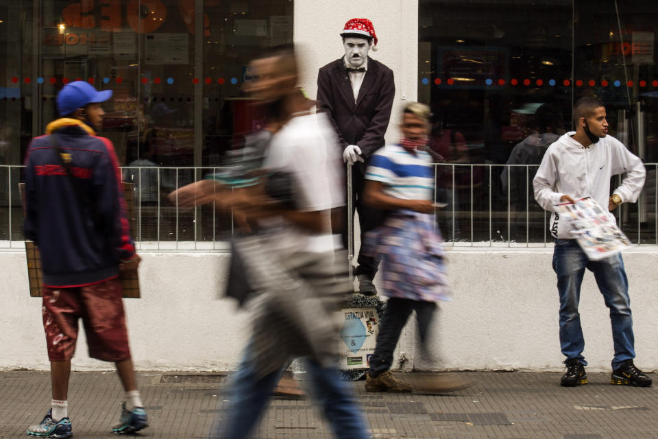 A street performer dressed as Charlie Chaplin stands still as he works for tips from shoppers along the street "25 de Marco" days before a COVID-19 lockdown goes into effect in Sao Paulo, Brazil, Wednesday, Dec. 23, 2020. Only essential business will be allowed to operate from Dec. 25 - 27 and Jan. 1 - 3. (AP Photo/Carla Carniel)