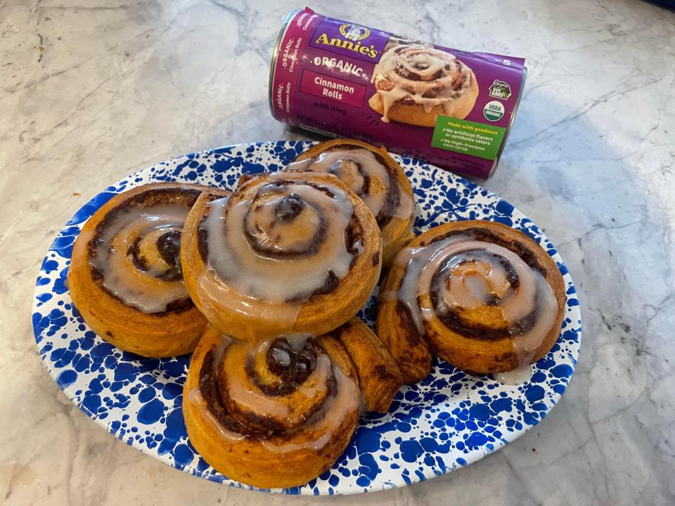 Baked cinnamon rolls with frosting on a plate. A container of Annie's Organic Cinnamon Rolls is in the background.