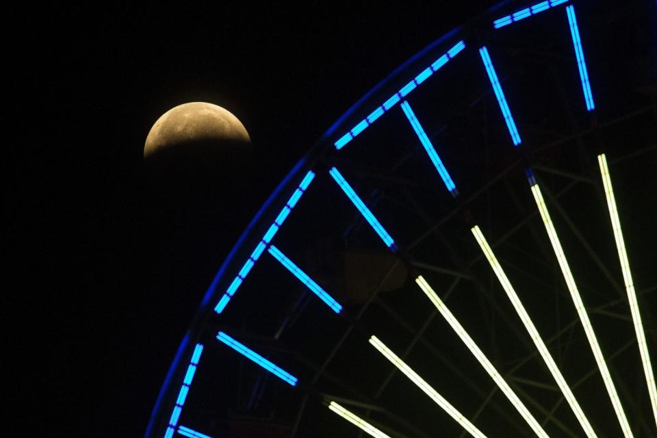 The bottom half of the moon is obscured by the Earth's shadow as seen from below the Ferris wheel at Santa Monica Pier