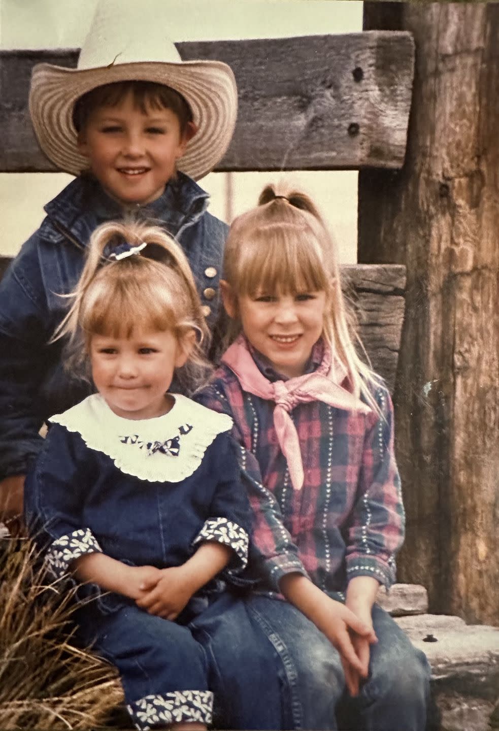 mackenzie porter with her brother and sister as children sitting in front of a rustic wood beam fence