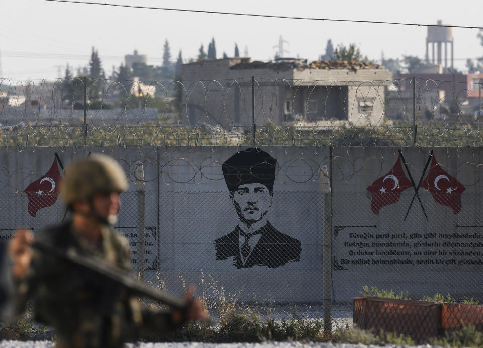 Shortly after the Turkish operation inside Syria had started and backdropped by a graffiti of modern Turkey's founder Mustafa Kemal Ataturk, a Turkish soldier stands on the Turkish side of the border in Akcakale, Sanliurfa province, southeastern Turkey, Wednesday, Oct. 9, 2019. Turkey launched a military operation Wednesday against Kurdish fighters in northeastern Syria after U.S. forces pulled back from the area, with a series of airstrikes hitting a town on Syria's northern border. (AP Photo/Lefteris Pitarakis)