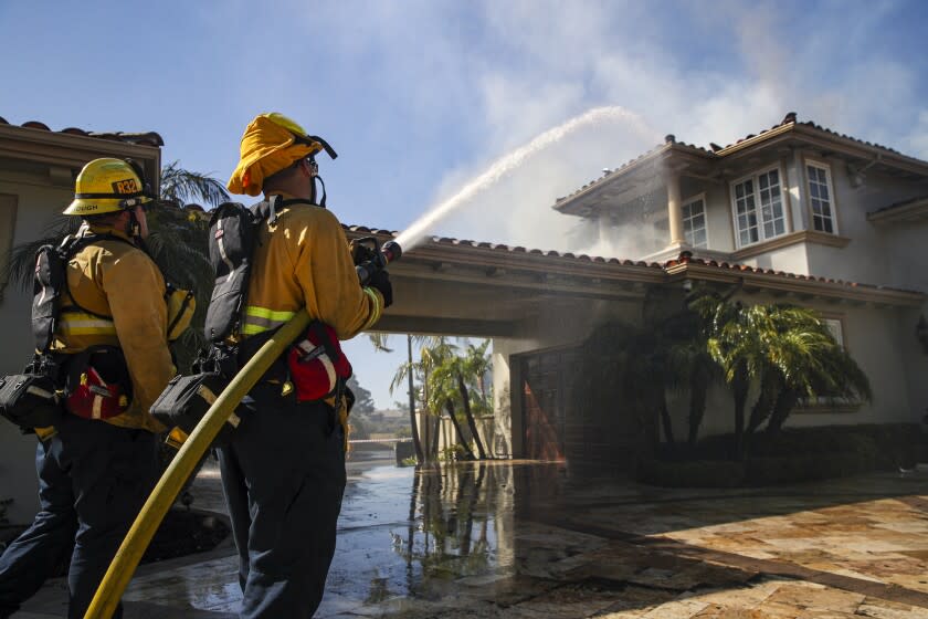 Laguna Niguel, CA - May 12: El Segundo firefighters Mathew Goodenough, left, and Javier Olmeda hose down a smoldering homes from the Coastal fire on Vista Court on Thursday, May 12, 2022 in Laguna Niguel, CA. (Irfan Khan / Los Angeles Times)