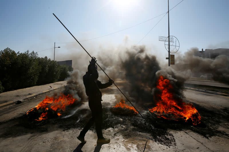 Iraqi demonstrator burns tires to block a road during ongoing anti-government protests in Najaf