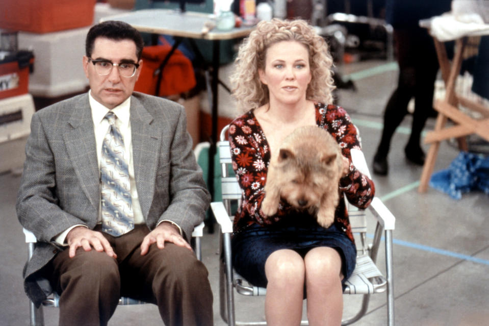 Eugene Levy and Catherine O'Hara sit side by side with a small dog on Catherine's lap in a scene from a film