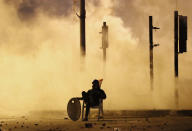 An anti-government protester covered by the smoke of the tear gas, sits on the middle of a street, during a protest against the new government, in downtown Beirut, Lebanon, Wednesday, Jan. 22, 2020. Lebanon's new government, made up of members nominated by the Shiite group Hezbollah and its allies got down to business Wednesday, a day after it was formed. Questions arose immediately about its ability to halt a spiral of economic and political collapse. (AP Photo/Hussein Malla)