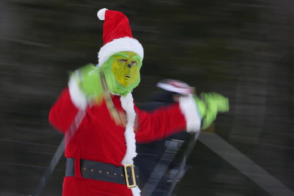 A skier dressed as the Grinch wearing a Santa Claus outfit skis for charity at the Sunday River Ski Resort, Sunday, Dec. 11, 2022, in Newry, Maine. (AP Photo/Robert F. Bukaty)