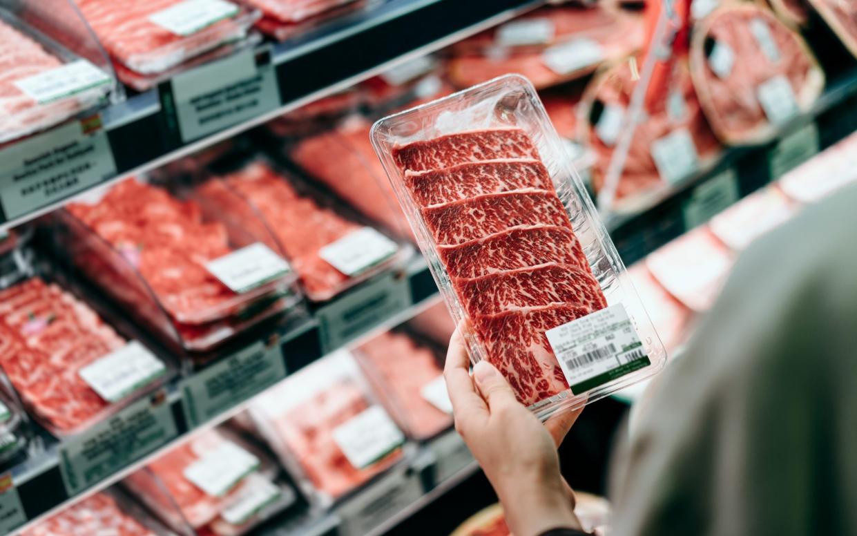 Over the shoulder view of woman shopping in a supermarket. She is choosing meat and holding a packet of organic beef in front of the refrigerated section