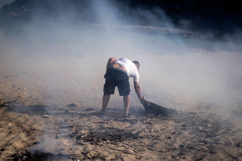 A local resident tries to extinguish a fire on the beach, near the seaside resort of Lindos, on the Aegean Sea island of Rhodes