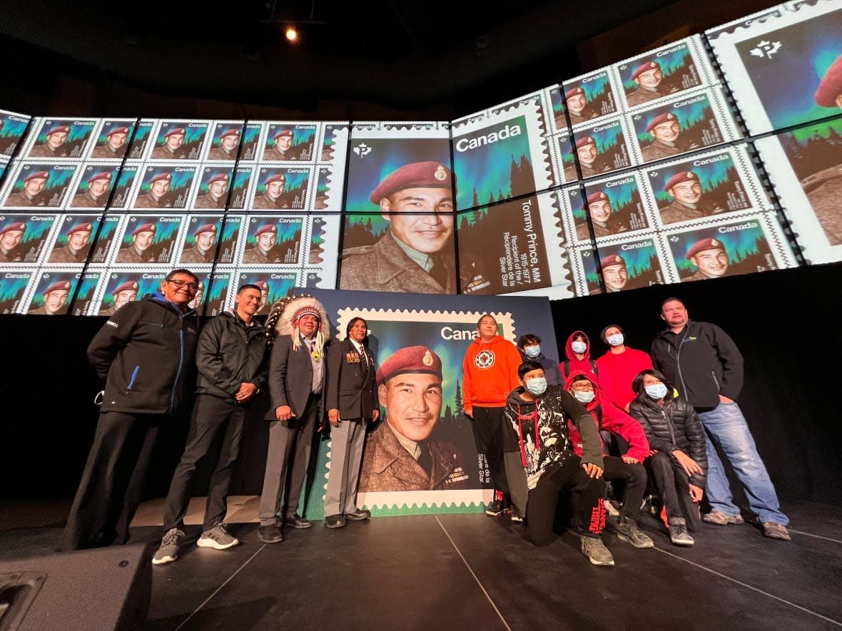 A group of people, including Brokenhead Ojibway Nation chief Gordon Bluesky (third from the left) and Tommy Prince Jr. (fourth from the left), pose in front of the newly unveiled stamp recognizing Sgt. Tommy Prince, who served in the Second World War and the Korean War. (Gary Solilak/CBC - image credit)