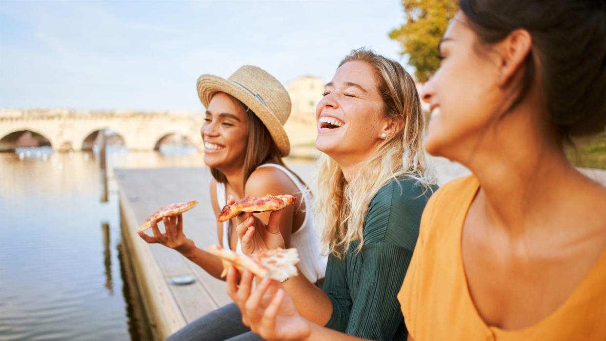 three beautiful women sitting on the stairs of the city streets eating pizza