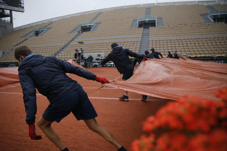 Stadium workers cover Suzanne Lenglen court after rain suspended the first round match of the French Open tennis tournament between Sofia Kenin of the U.S. and Russia's Liudmila Samsonova at the Roland Garros stadium in Paris, France, Tuesday, Sept. 29, 2020. (AP Photo/Christophe Ena)