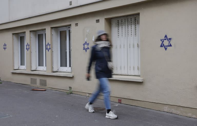 A woman walks along a building whose facade is covered with Stars of David painted during the night, in the Alesia district of Paris, on October 31, 2023. (Photo by Geoffroy Van der Hasselt / AFP)