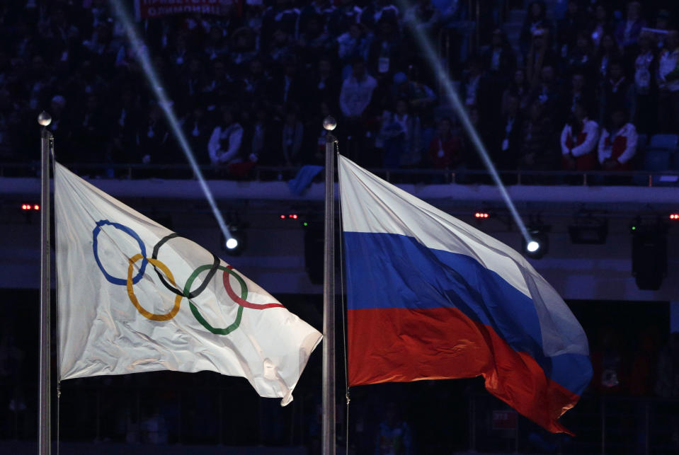 FILE - In this Feb. 23, 2014 file photo, the Russian national flag, right, flies after next to the Olympic flag during the closing ceremony of the 2014 Winter Olympics in Sochi, Russia. The World Anti-Doping Agency banned Russia on Monday Dec. 9, 2019 from the Olympics and other major sporting events for four years, though many athletes will likely be allowed to compete as neutral athletes. (AP Photo/Matthias Schrader, File)