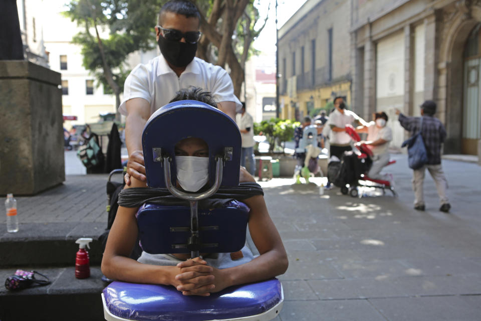 Roberto is getting a massage in the street in Mexico City, Saturday, Dec. 18, 2020. After months of resisting to avoid hurting the economy, officials banned all non-essential activities starting Saturday and returned to a partial lockdown in Mexico City and the surrounding State of Mexico because of a spike in coronavirus cases that has crowded hospitals. (AP Photo/Ginnette Riquelme)