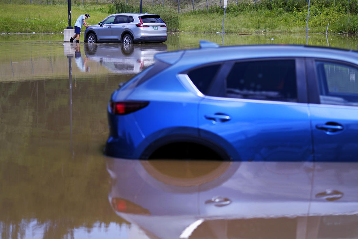 A man walks through floodwaters by two submerged cars.