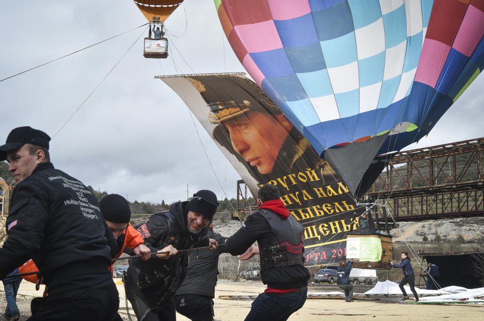 Enthusiasts fix a portrait of Russian President Vladimir Putin to a balloon during thecelebration of the anniversary of Crimea annexation from Ukraine in 2014, in Sevastopol, Crimea, Thursday, March 18, 2021. Residents of cities in Crimea and Russia are holding gatherings to commemorate the seventh anniversary of Russia's annexation of the Black Sea peninsula from Ukraine. The sign reading "Another gave us back the cradle of baptism. March 18, 2014". (AP Photo)