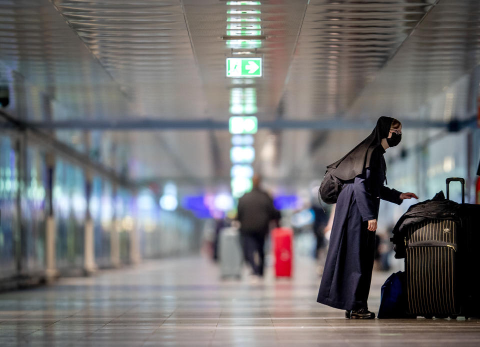 A nun wearing a face mask stands next to her baggage at the airport in Frankfurt, Germany, Tuesday, March 30, 2021. (AP Photo/Michael Probst)