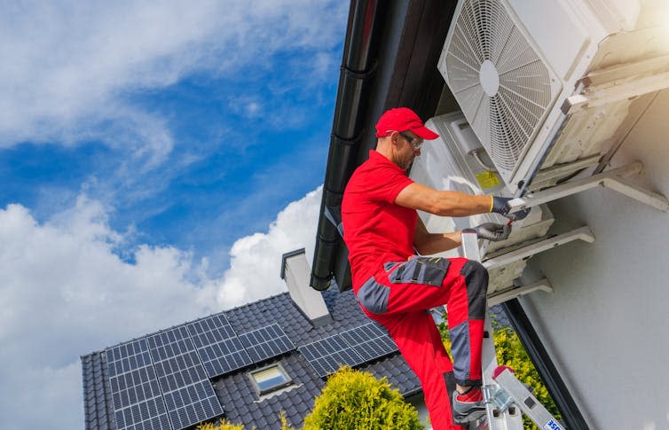 An engineer adjusts a heat pump on the exterior of a house.