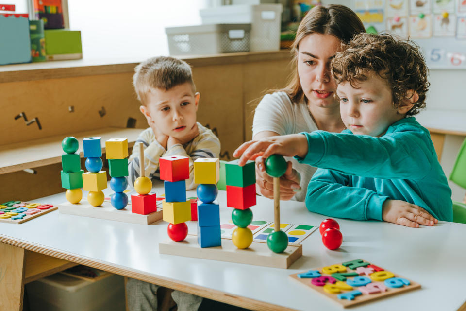 Female teacher helping little boy sort the cubes by color in a kindergarten. Early development concept. Selective focus.�