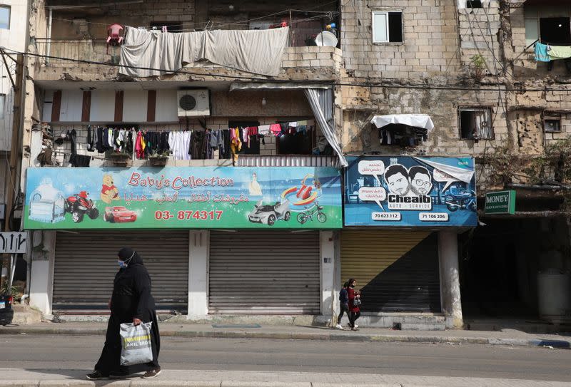 A woman wearing a face mask walks near closed shops in Chiyah