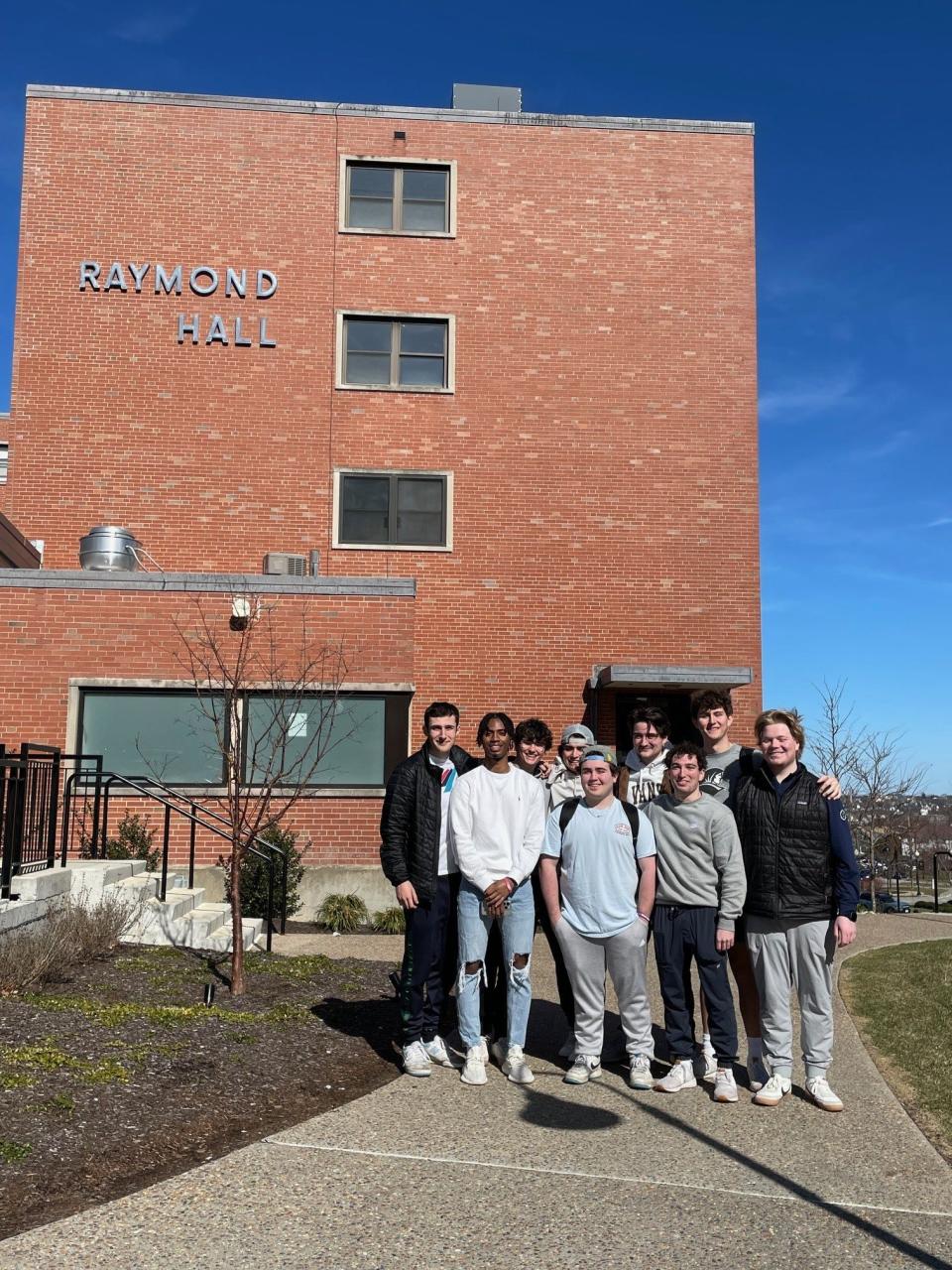 Providence College students, including Daniel Singh, front left, and Brandon Reichert, front right, who helped raise funds to send security guard James Mogaji to see family in Liberia stand in front of Raymond Hall, where they live and Mogaji works.