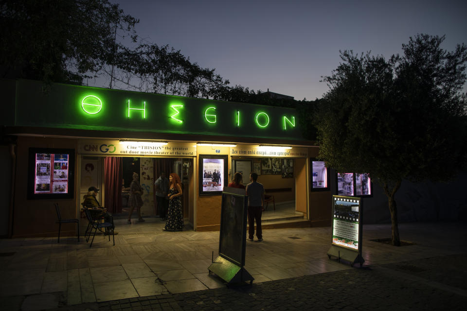 In this Thursday June 4 , 2020 photo passers by looks at movie notices outside the Thision outdoor summer cinema where moviegoers watch films under the ancient Acropolis. Cine Thision is one of the oldest open-air movie theaters in Athens, built in 1935. (AP Photo/Petros Giannakouris)