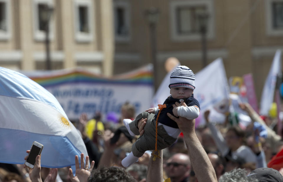 A man lifts a baby up as he waits for Pope Francis to recite the Regina Coeli prayer from the window of his studio overlooking St. Peter's Square, at the Vatican, Sunday, May 4, 2014. (AP Photo/Alessandra Tarantino)