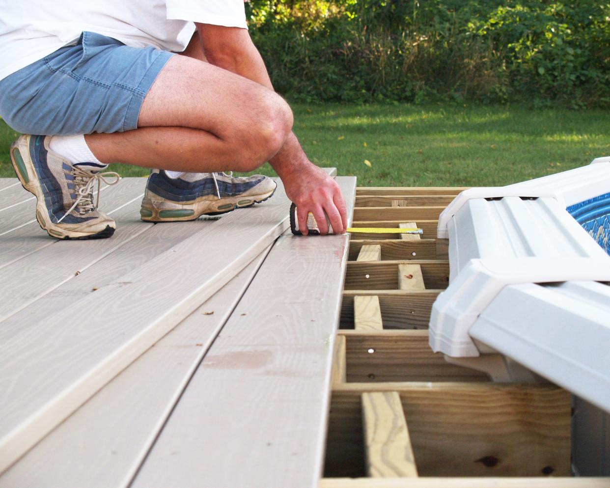 Man measuring boards while building a new above-ground pool deck with the yard in the background