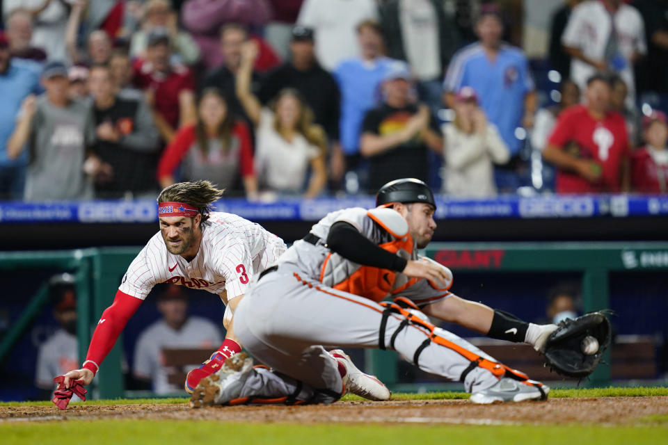 Philadelphia Phillies' Bryce Harper, left, scores the game-winning run past Baltimore Orioles catcher Austin Wynns on a two-run triple by J.T. Realmuto during the 10th inning of an interleague baseball game, Tuesday, Sept. 21, 2021, in Philadelphia. (AP Photo/Matt Slocum)