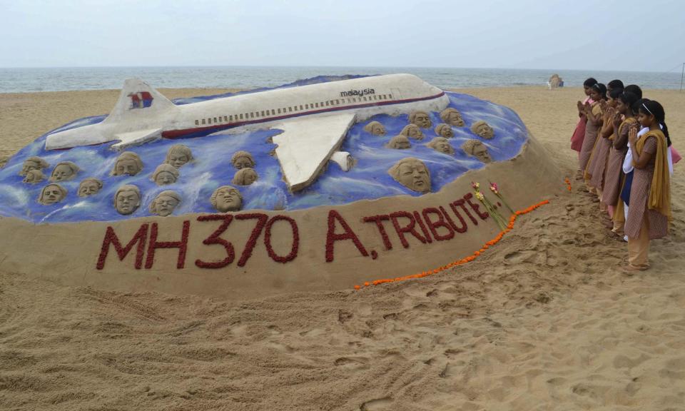 Schoolgirls pray next to a sand art sculpture created by Indian sand artist Sudarshan Patnaik to pay tribute to the passengers and crew onboard the missing Malaysia Airlines flight MH370, on a beach in Puri