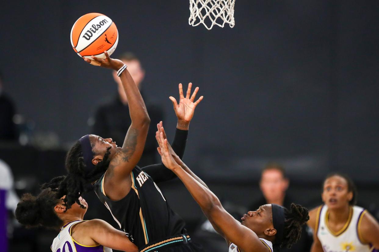 A basketball player shoots as she leaps above multiple hands trying to block her.