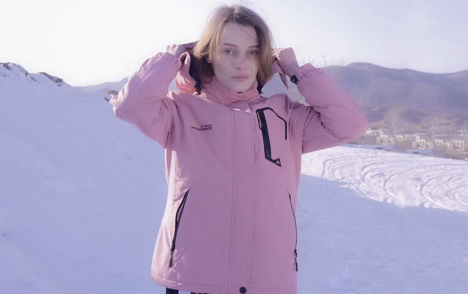 person wearing a pink ski jacket, lifting the hood