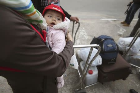 A Palestinian woman returning to Gaza carries her child at the Rafah border crossing between Egypt and southern Gaza Strip November 26, 2014. REUTERS/Ibraheem Abu Mustafa