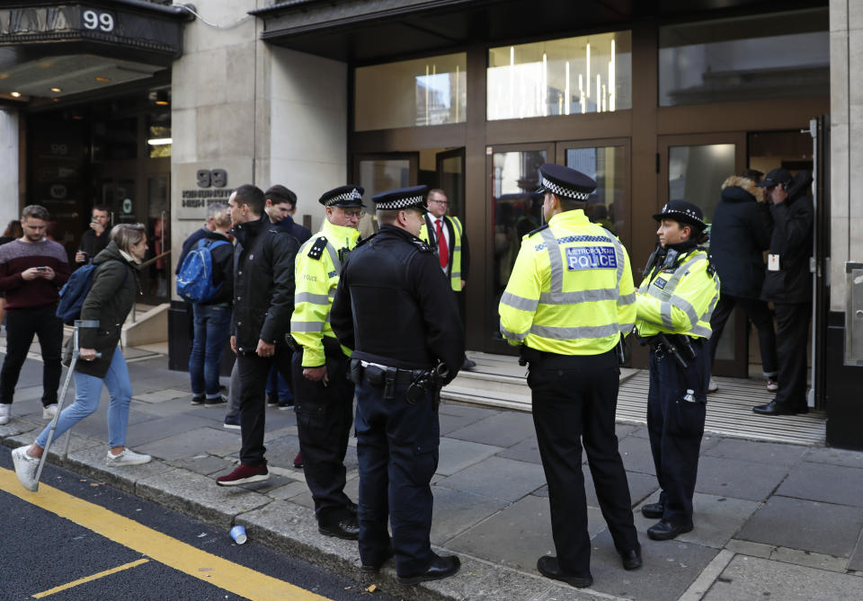 Police officers and security watch as people re-enter a building after a stabbing incident in central London, Friday, Nov. 2, 2018. British police say two people have been stabbed and a man has been arrested at an address in central London that is home to the offices of Sony Music. (AP Photo/Alastair Grant)