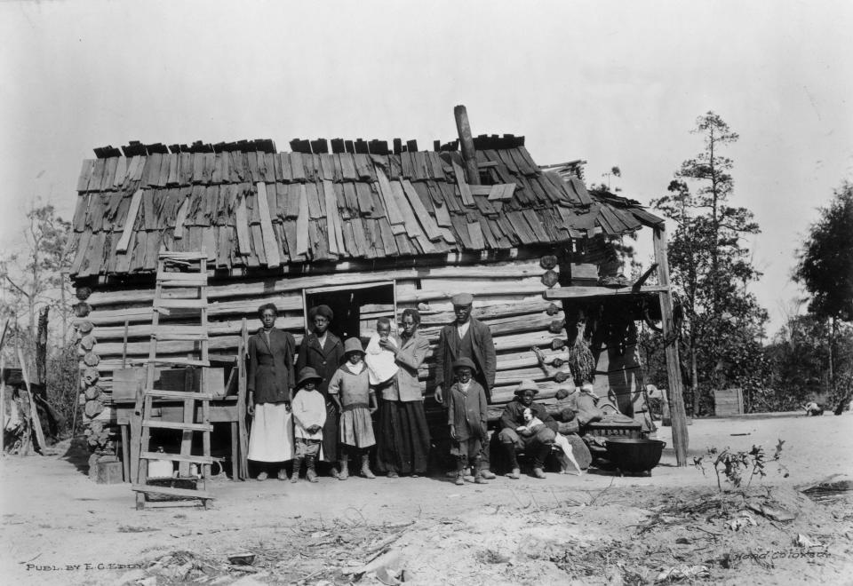 Great Depression large African American family poses in front of log cabin