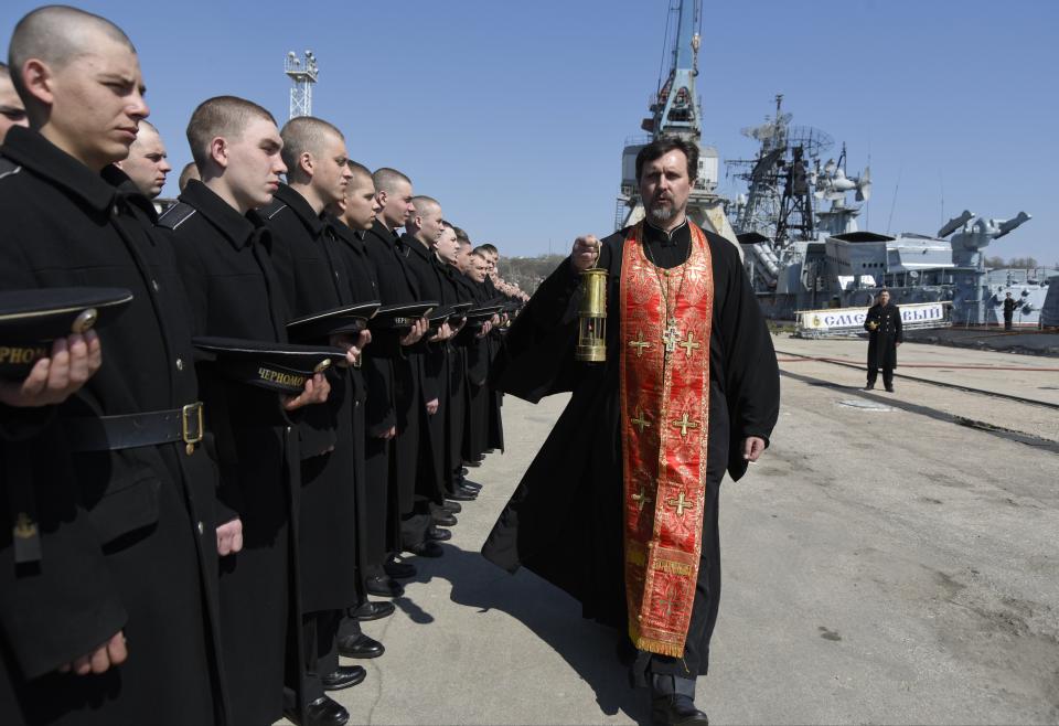 FILE - A Russian Orthodox priest carries the Holy Fire which was delivered to the Easter service with Russian Black Sea fleet sailors in Sevastopol, Crimea, April 12, 2015, with a Russian Navy Ship in the background. Successful Ukrainian drone and missile strikes have provided a major morale boost for Kyiv at a time when its undermanned and under-gunned forces are facing Russian attacks along the more than 1,000-kilometer front line. Challenging Russia’s naval superiority also has helped create more favorable conditions for Ukrainian grain exports and other shipments from the country’s Black Sea ports. (AP Photo/File)