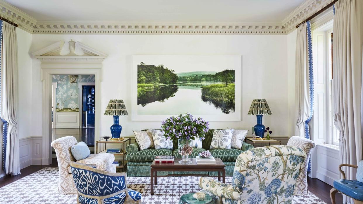 a serene landscape photograph relaxes grand moldings with a masterful new modernity and the walls are white and there is a green velvet sofa