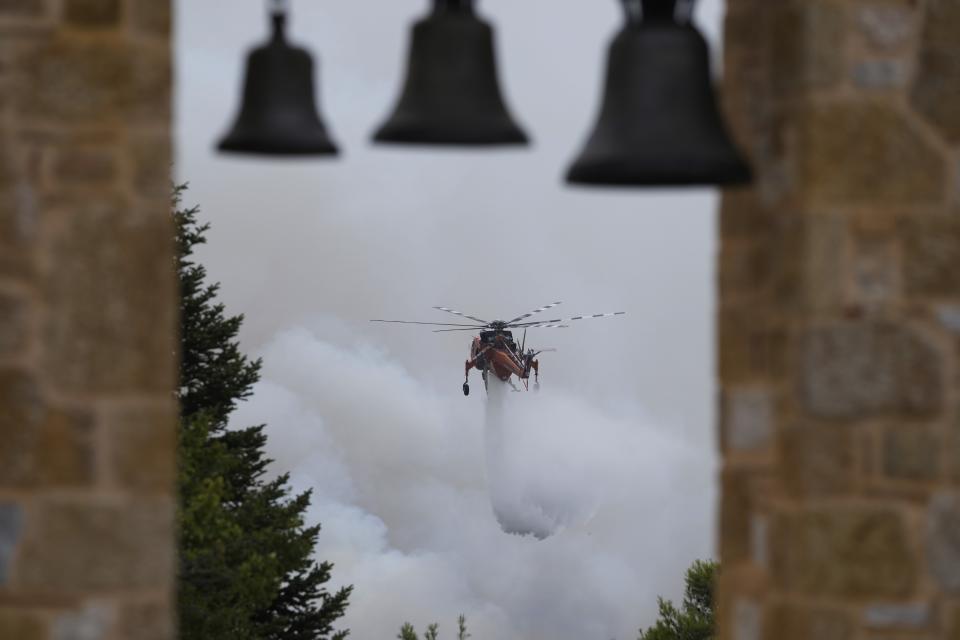 An helicopter drops water over a fire in Ippokratios Politia village, about 35 kilometres (21 miles) north of Athens, Greece, Friday, Aug. 6, 2021. Thousands of residents of the Greek capital have fled to safety from a wildfire that burned for a fourth day north of Athens as crews battle to stop the flames reaching populated areas, electricity installations and historic sites. (AP Photo/Thanassis Stavrakis)