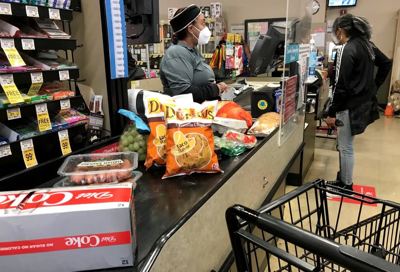 LONG BEACH, CALIF. - DEC. 16, 2020. A cashier helps a customer at the checkout stand in the Von's grocery store iin Long Beach on Wednesday, Dec. 16, 2020. (Luis Sinco/Los Angeles Times)