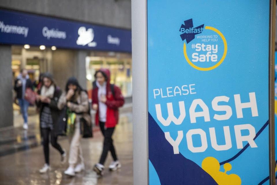 Young people walk past a Covid safety message from Belfast City Council (Liam McBurney/PA) (PA Wire)