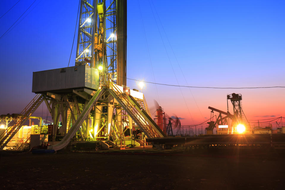 Drilling rigs lit up at dusk.