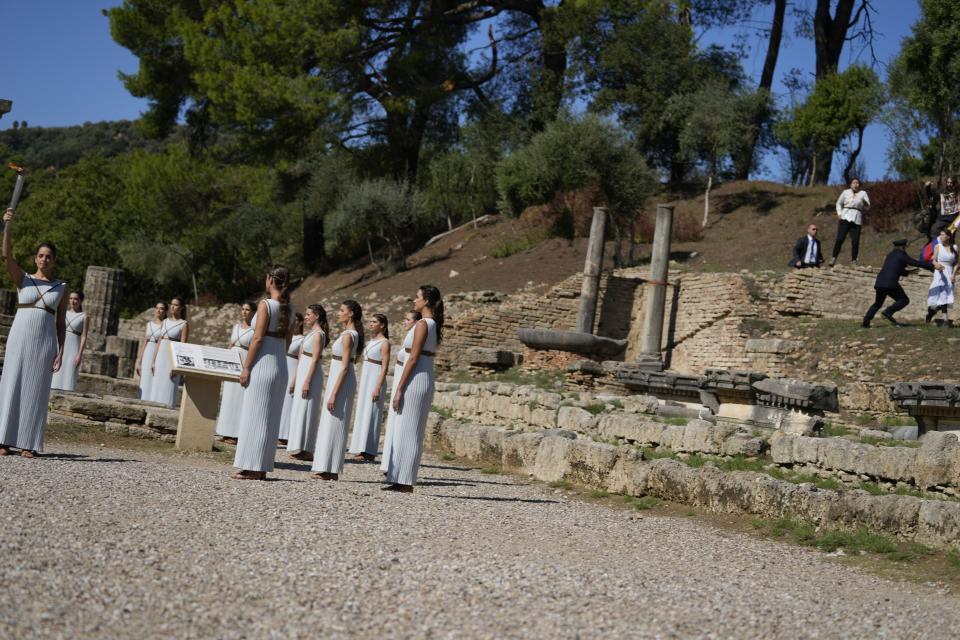 Greek actress Xanthi Georgiou, left, playing the role of the High Priestess, holds the torch as police officers, right, run to detain pro-democracy protesters at the lighting of the Olympic flame at Ancient Olympia site, birthplace of the ancient Olympics in southwestern Greece, Monday, Oct. 18, 2021. The flame will be transported by torch relay to Beijing, China, which will host the Feb. 4-20, 2022 Winter Olympics. (AP Photo/Thanassis Stavrakis)