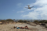 A woman sunbathes on the beach as an airplane lands at the Balearic Islands capital of Palma de Mallorca, Spain, Wednesday, July 29, 2020. Concerns over a new wave of coronavirus infections brought on by returning vacationers are wreaking havoc across Spain's tourism industry, particularly in the Balearic Islands following Britain's effective ban on travel to the country. (AP Photo/Joan Mateu