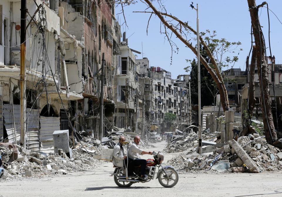 Two men ride a motorbike along a destroyed street in Douma (Getty Images)