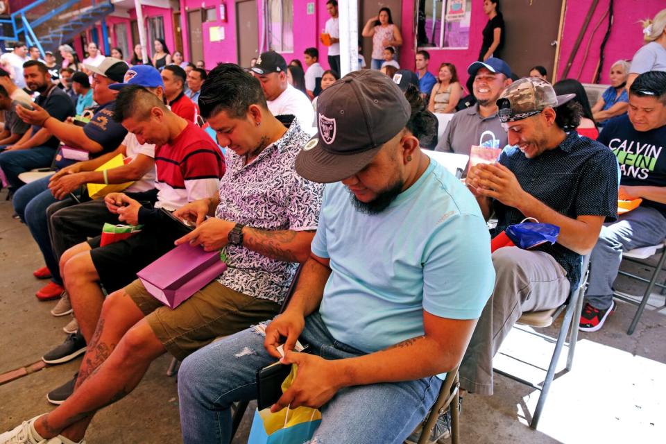 Men sit in chairs while they each look through a wallet with money in it.