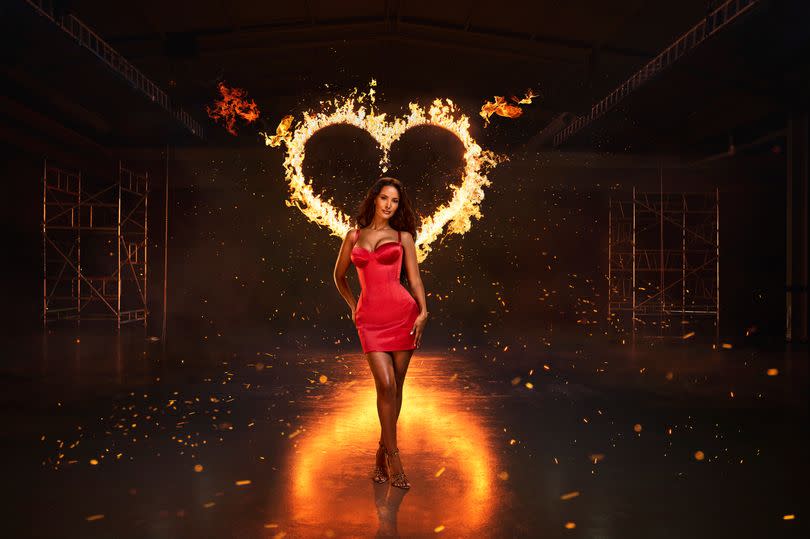Maya Jama in a red dress under a large heart which is on flames